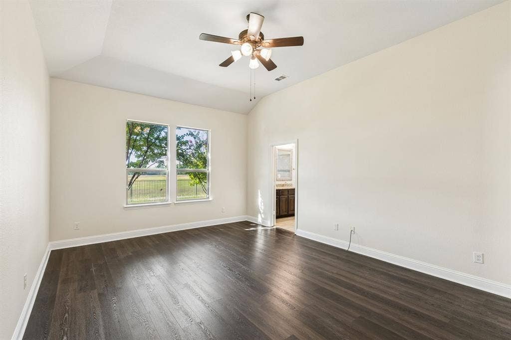 Vaulted ceiling with a ceiling fan, dual windows, wood-finish flooring, and white trim