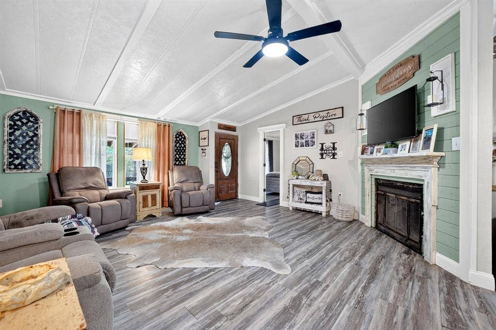 302 Longleaf Street, Gun Barrel City, TX 75156 Vaulted ceilings with exposed beams, wood-finish flooring, accent wall with shiplap detail, decorative fireplace with mantel, and a built-in ceiling fan with lighting