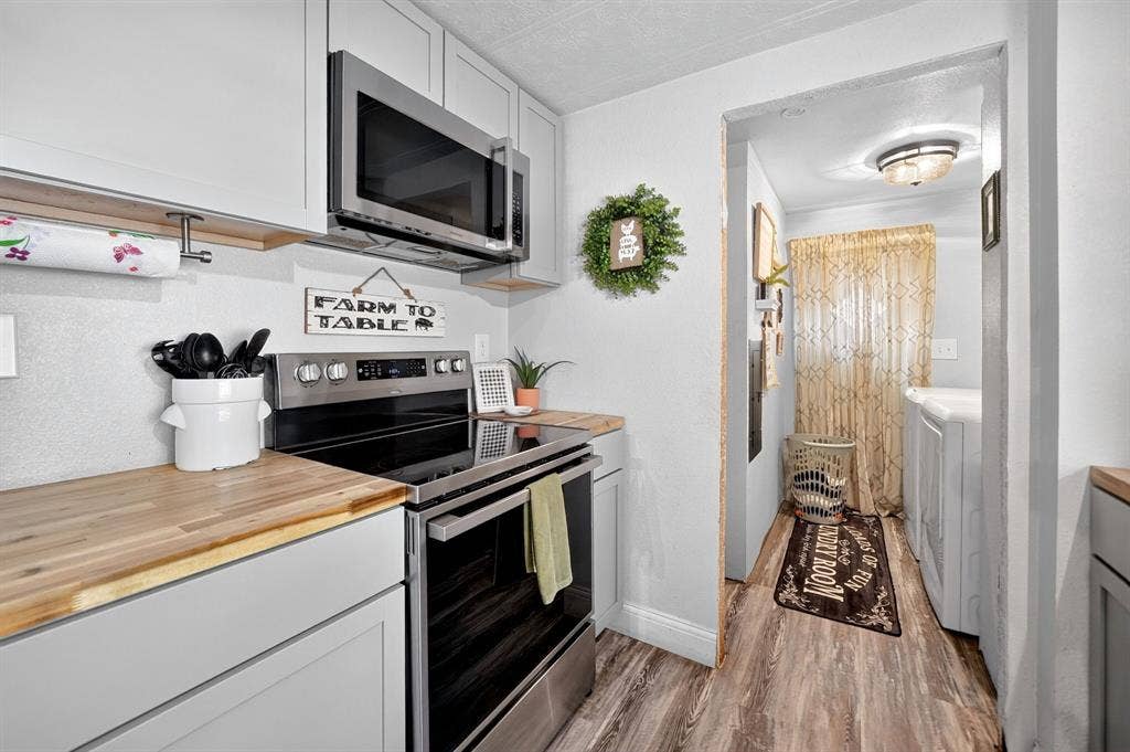 302 Longleaf Street, Gun Barrel City, TX 75156 White upper and lower cabinetry, wood-finish countertops, stainless steel microwave, and a stainless steel range with a flat cooktop