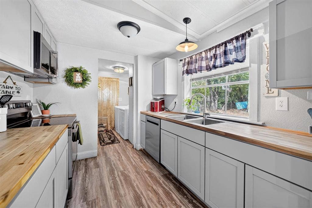 302 Longleaf Street, Gun Barrel City, TX 75156 Galley kitchen featuring wood-finish countertops, stainless steel appliances, white cabinetry, a double basin sink, and wood-finish flooring