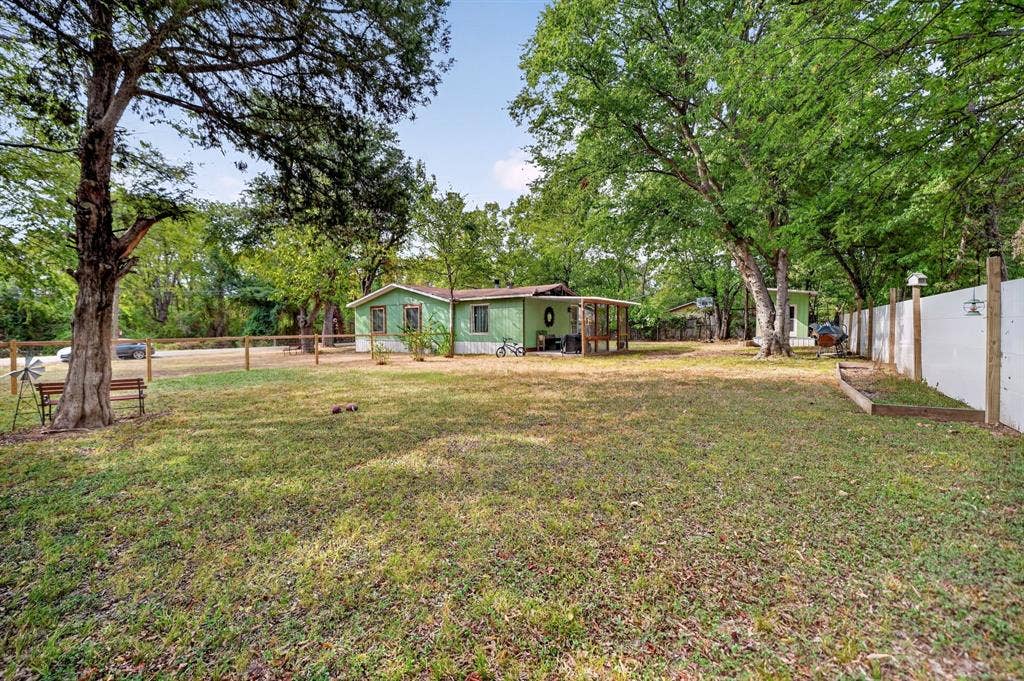 302 Longleaf Street, Gun Barrel City, TX 75156 Expansive grassy yard framed by mature trees, featuring a white privacy fence and a wood fence