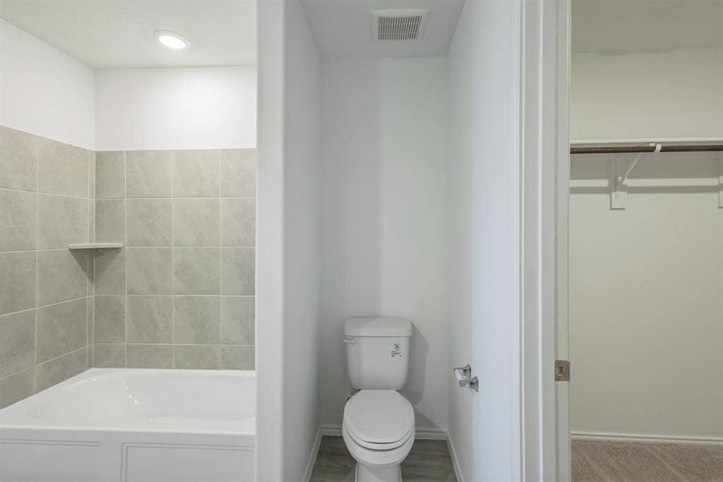 7904 Thornton Drive, McKinney, TX 75071 Bathtub with tiled surround and integrated shelf, recessed lighting, toilet with wall-mounted toilet paper holder, wood-finish flooring, and a closet with a hanging rod