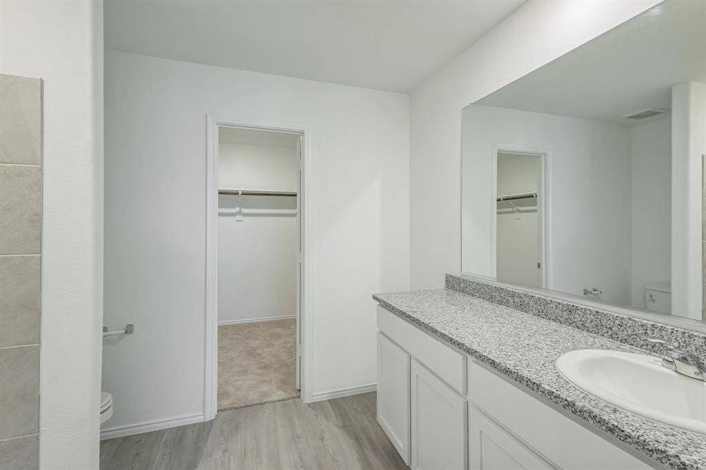 7904 Thornton Drive, McKinney, TX 75071 Wood-finish flooring, vanity with white cabinetry, integrated sink, and stone-finish countertop