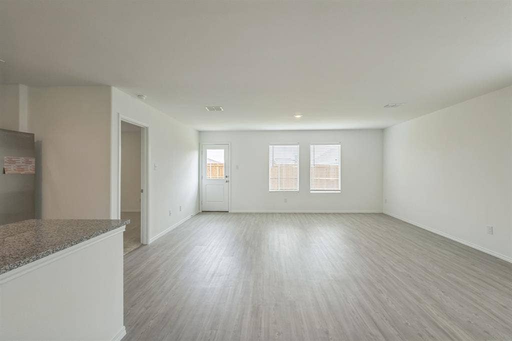 7904 Thornton Drive, McKinney, TX 75071 Spacious open-concept area featuring wood-finish flooring, white walls, multiple windows with blinds, and a rear exterior door