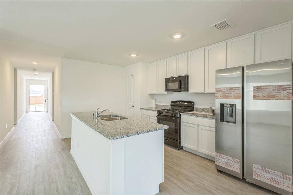 7904 Thornton Drive, McKinney, TX 75071 Kitchen featuring white cabinetry, granite-style countertops, an island with an integrated sink, and stainless steel appliances