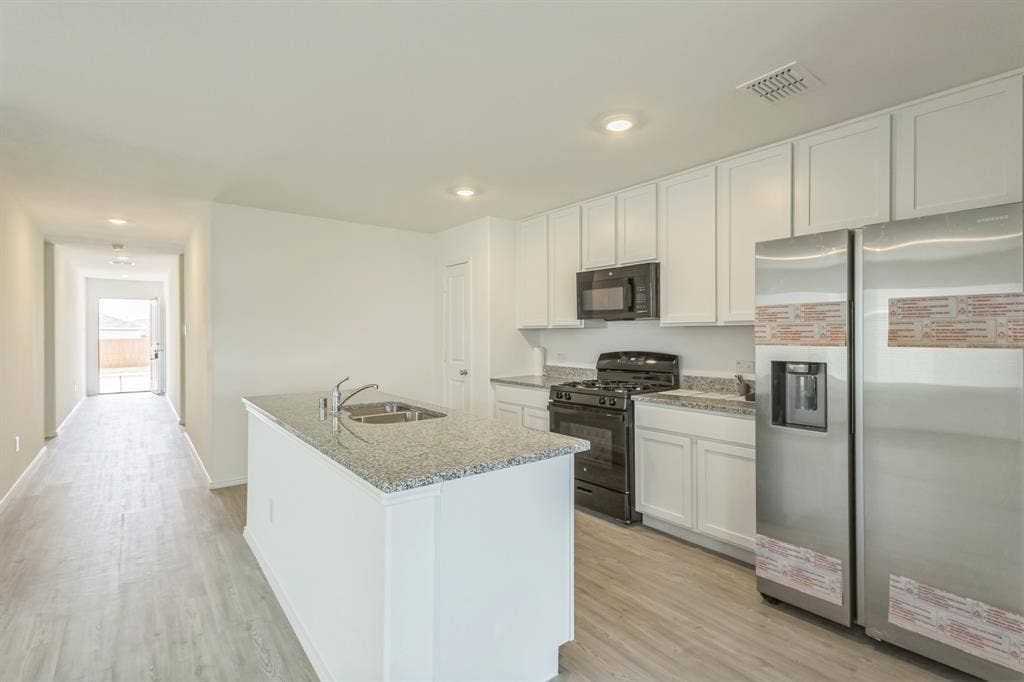 7904 Thornton Drive, McKinney, TX 75071 Kitchen featuring white cabinetry, granite countertops, stainless steel appliances, and a central island with an undermount sink