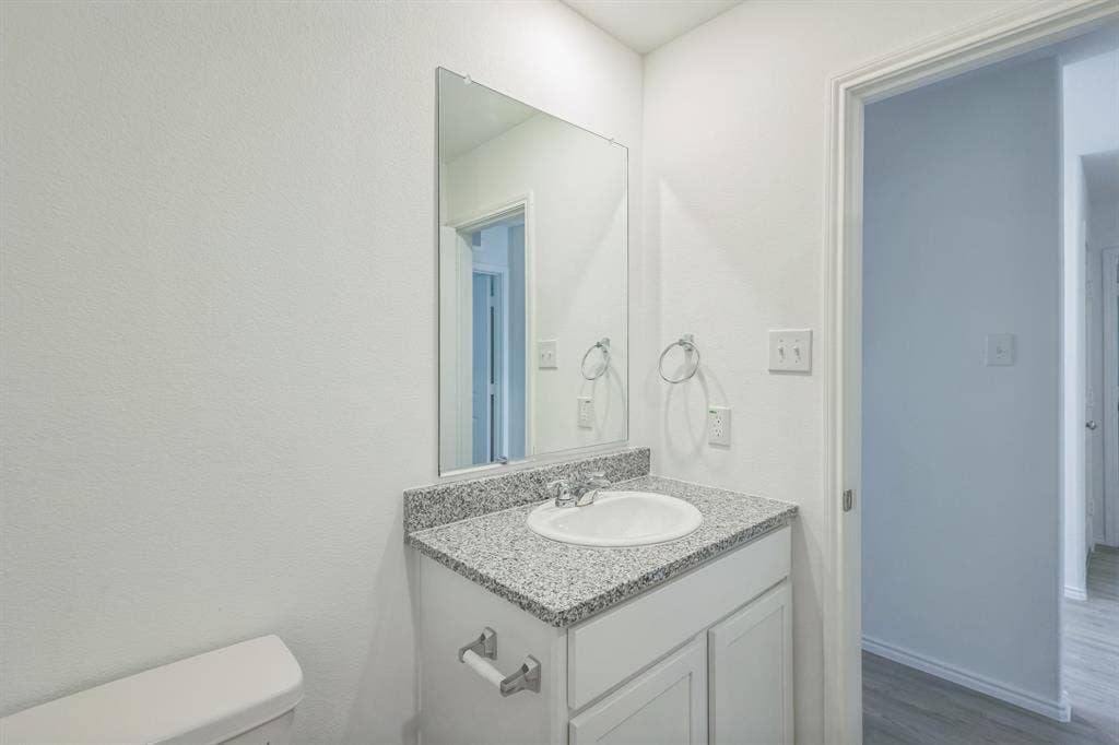 7904 Thornton Drive, McKinney, TX 75071 Bathroom featuring a vanity with a granular countertop, an integrated sink, a wall-mounted mirror, and a two-door cabinet