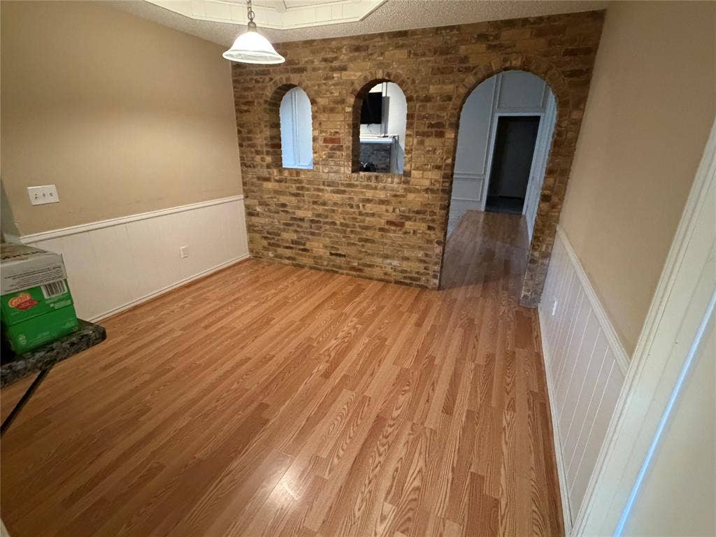 3912 Bandera Drive, Plano, TX 75074 Hardwood-finish flooring, brick accent wall with arched openings, white paneled wainscoting, and a built-in ceiling light fixture