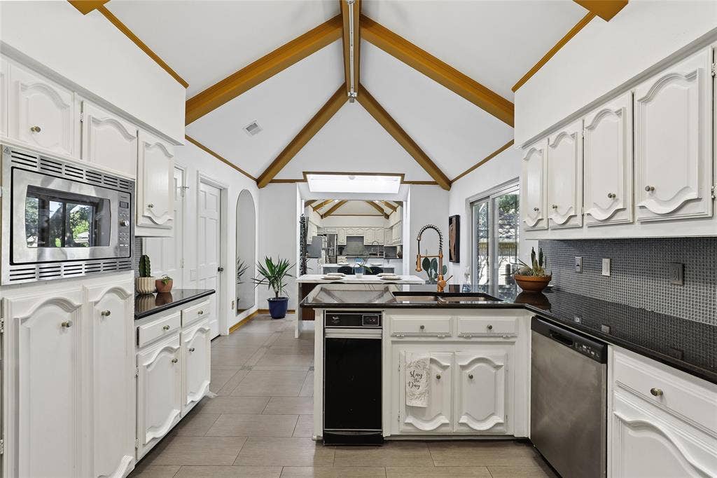 5716 Plumtree Drive, Dallas, TX 75252 Vaulted ceilings with exposed wood beams, white cabinetry, dark countertops, built-in stainless steel microwave, and tile flooring