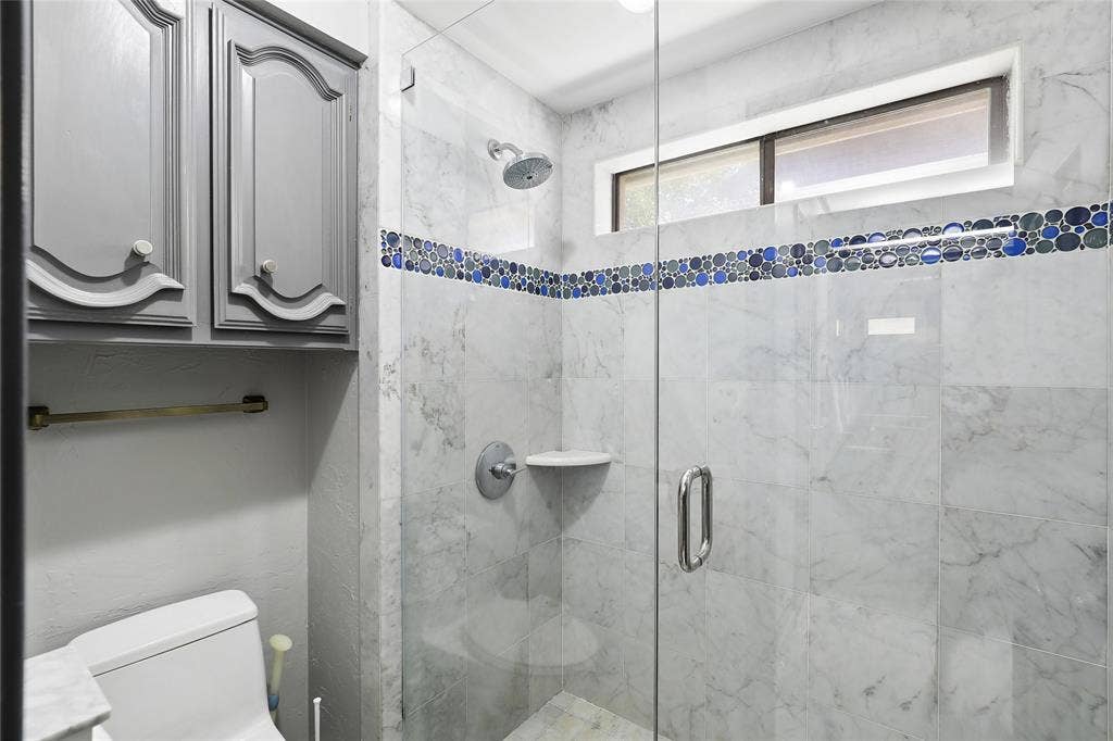 5716 Plumtree Drive, Dallas, TX 75252 Frameless glass-enclosed shower with full height marble-look tiling and mosaic accent. Jack and jill ensuite bathroom.