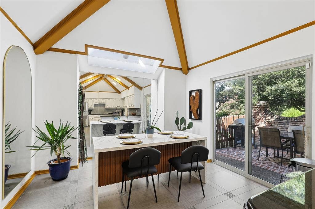 5716 Plumtree Drive, Dallas, TX 75252 Vaulted ceilings with exposed wood beams, skylight, and sliding glass door to an outdoor patio with brick wall and patterned tile