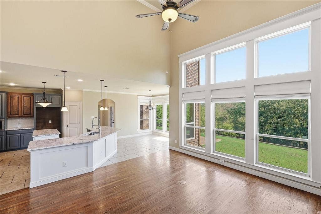 3110 Creek Haven Drive, Highland Village, TX 75077 Vaulted ceiling with integrated paddle fan, expansive multi-pane windows, wood-finish flooring, and kitchen featuring a stone-surface island and built-in cabinetry
