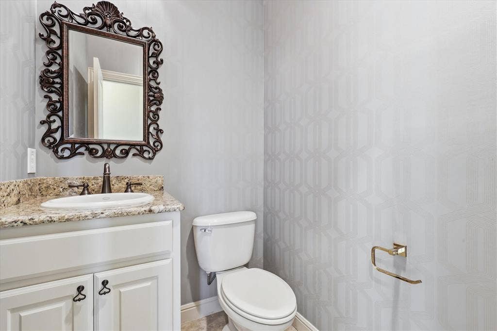 3110 Creek Haven Drive, Highland Village, TX 75077 Powder room featuring a white vanity cabinet with stone countertop, drop-in sink, ornate wall mirror, and textured wallpaper