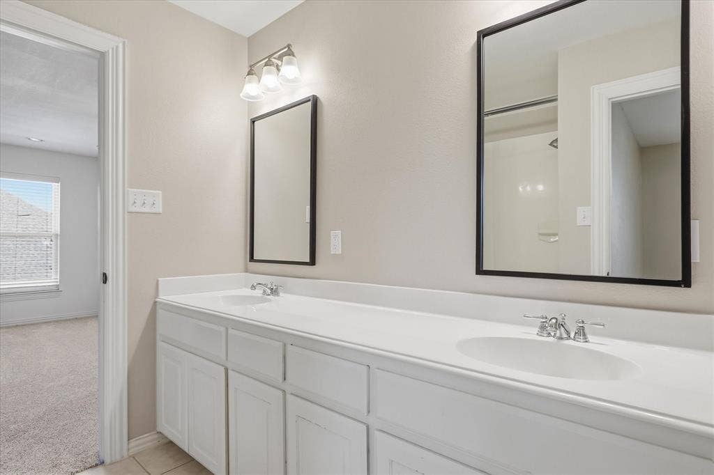 3110 Creek Haven Drive, Highland Village, TX 75077 Double vanity featuring white cabinetry, integrated dual-basin countertop, black-framed mirrors, and polished chrome faucets