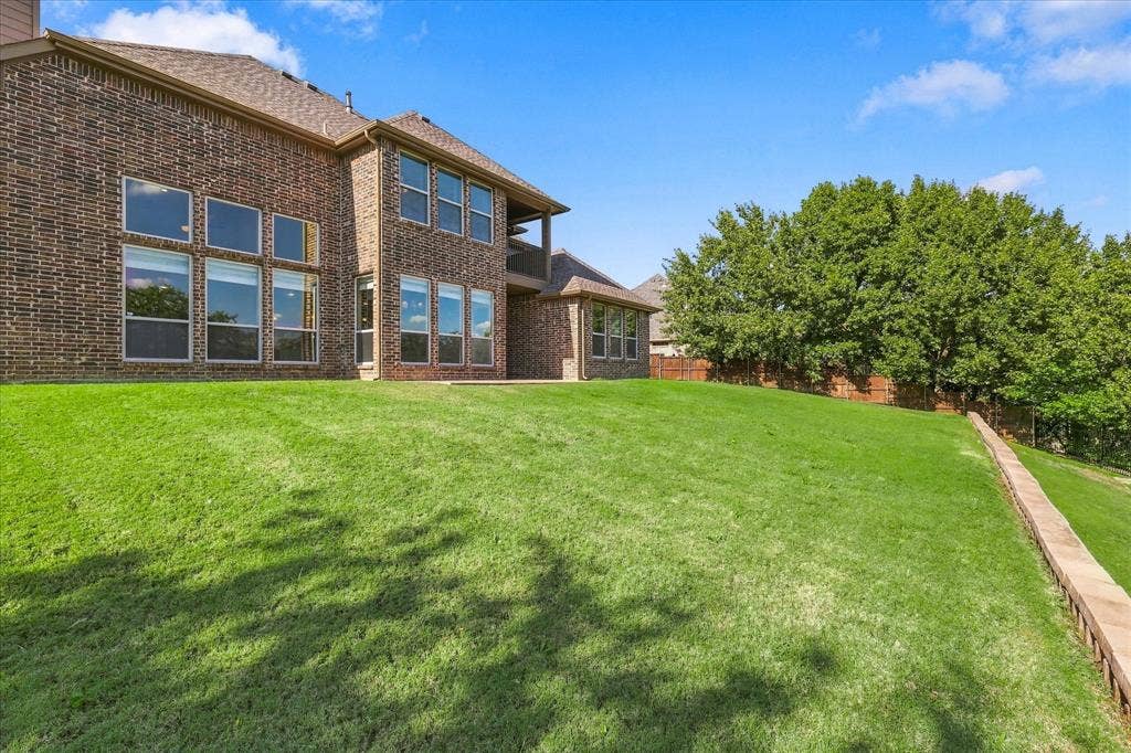 3110 Creek Haven Drive, Highland Village, TX 75077 Multi-level brick exterior featuring expansive windows and a large manicured lawn with a stone retaining wall