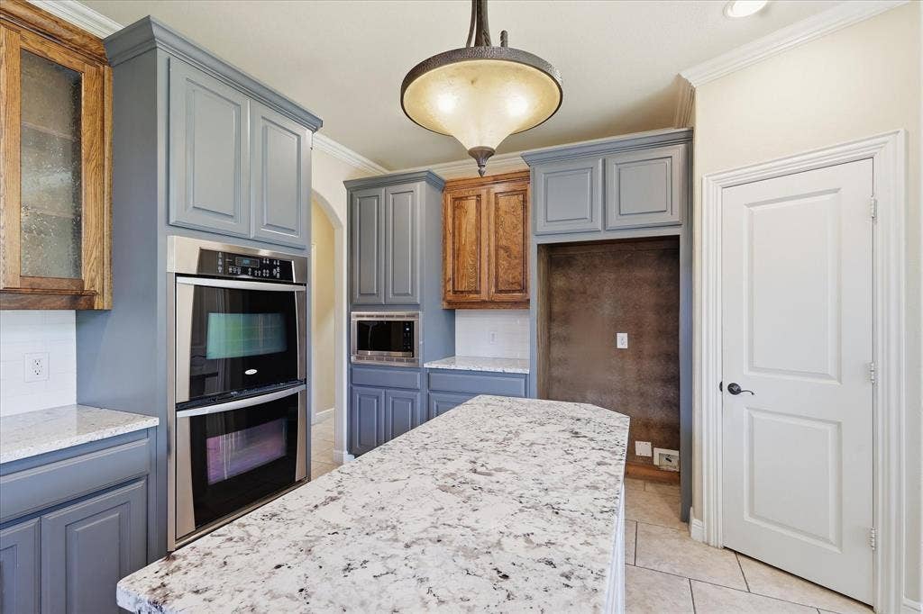 3110 Creek Haven Drive, Highland Village, TX 75077 Kitchen featuring slate-blue and natural wood-tone cabinetry, speckled stone countertops, a stainless steel double wall oven, and a pendant light fixture