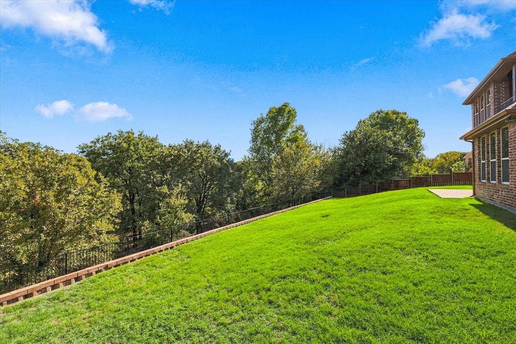 3110 Creek Haven Drive, Highland Village, TX 75077 Expansive backyard featuring a sloping grass lawn, tiered retaining wall, perimeter fencing, and mature trees