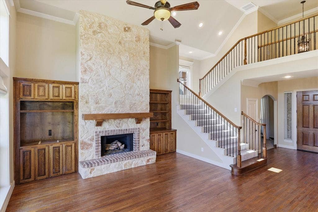 3110 Creek Haven Drive, Highland Village, TX 75077 Floor-to-ceiling stone fireplace with wood mantel, custom built-in cabinetry, wood-finish flooring, vaulted ceiling, and staircase with wooden railing