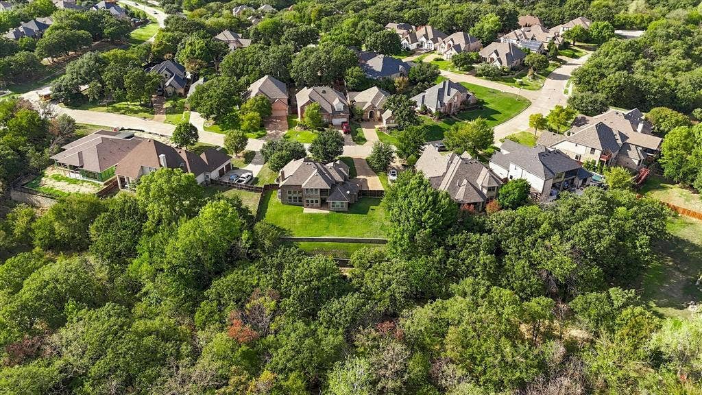 3110 Creek Haven Drive, Highland Village, TX 75077 Aerial perspective of a multi-story residence featuring a steep-pitched roofline, stone exterior facade, and a grass-covered backyard bordering a dense treeline