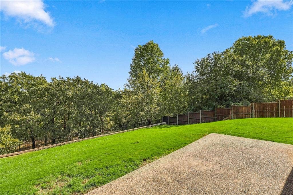 3110 Creek Haven Drive, Highland Village, TX 75077 Expansive backyard featuring a manicured lawn, exposed aggregate patio, wood privacy fencing, and mature trees