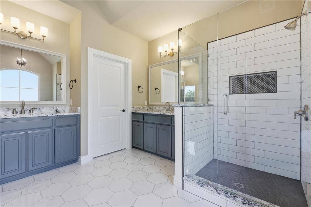 3110 Creek Haven Drive, Highland Village, TX 75077 Dual blue-toned vanities featuring stone-finish countertops, glass-enclosed shower with subway tile surround, and hexagonal tile flooring