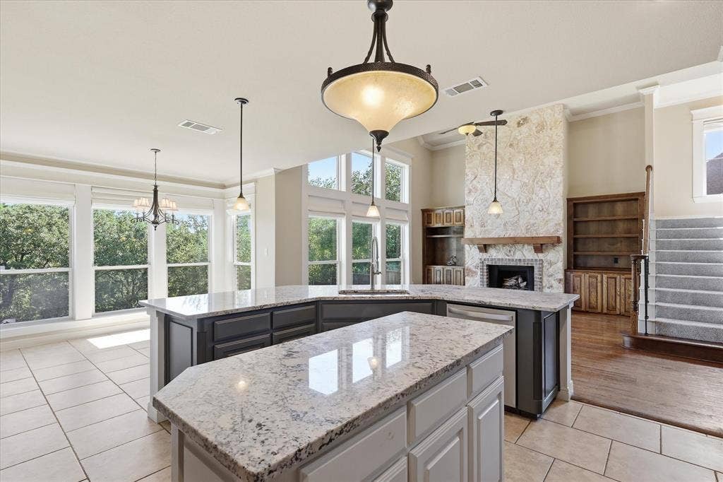 3110 Creek Haven Drive, Highland Village, TX 75077 Kitchen island featuring stone countertops and dual-tone cabinetry, floor-to-ceiling stone fireplace, built-in wooden shelving, and expansive windows