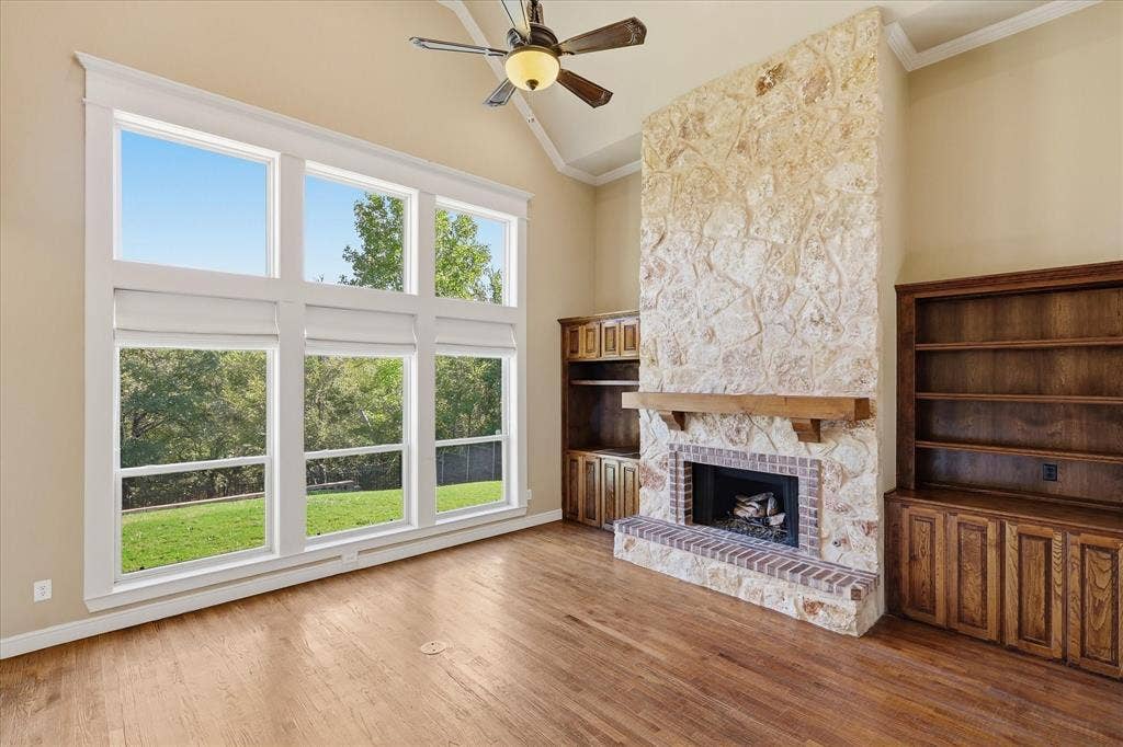 3110 Creek Haven Drive, Highland Village, TX 75077 Vaulted ceiling with a central fan, large multi-pane windows, floor-to-ceiling stone fireplace with a wood mantel, and custom wood-finish built-in cabinetry