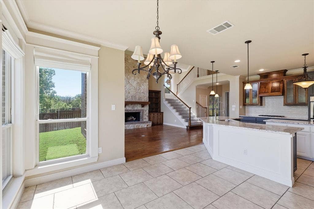 3110 Creek Haven Drive, Highland Village, TX 75077 Open-concept space featuring stone-facade fireplace, wood-finish flooring, tile flooring, tiered center island with countertop, and classic chandelier lighting