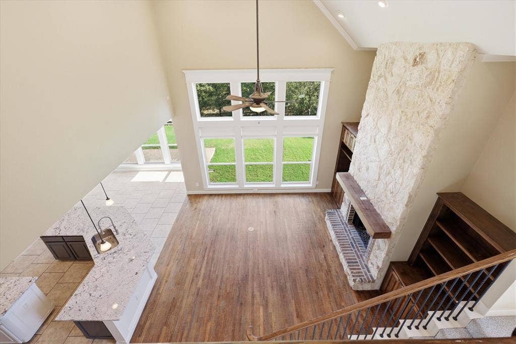 3110 Creek Haven Drive, Highland Village, TX 75077 Vaulted ceilings, floor-to-ceiling stone fireplace with a wood mantel, wood-finish flooring, expansive multi-pane windows, and built-in cabinetry