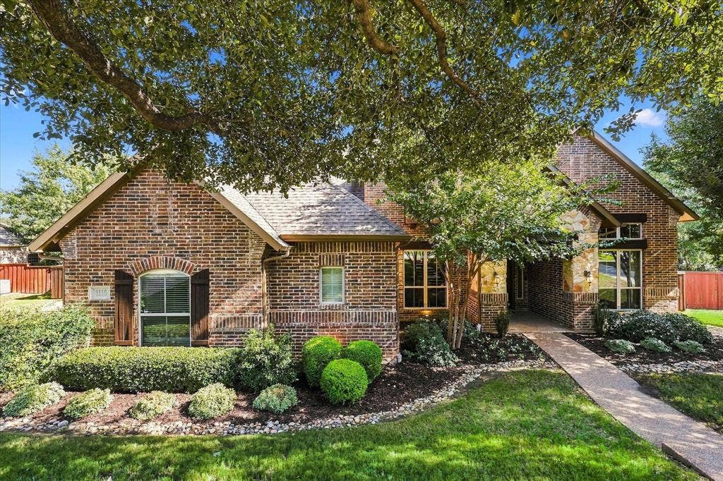 3110 Creek Haven Drive, Highland Village, TX 75077 Traditional brick exterior featuring stone accents, arched windows with shutters, a multi-gabled roofline, and a paved walkway