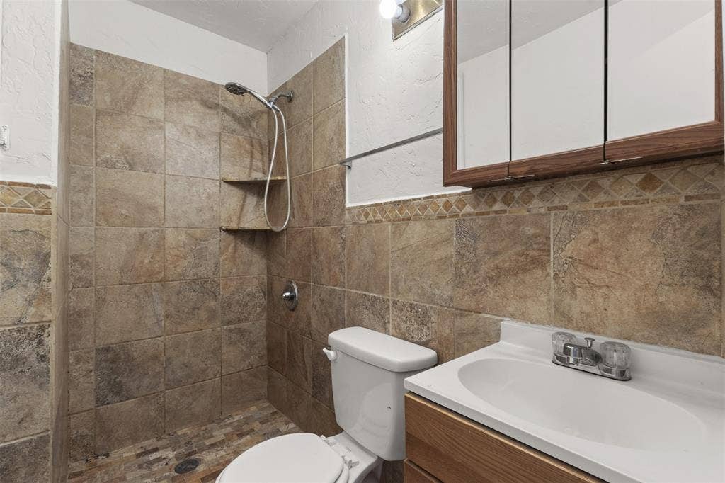 2563 Wood Valley Drive, Dallas, TX 75211 Tiled shower with built-in shelving, a vanity with an integrated sink, a medicine cabinet, and a decorative tile accent band