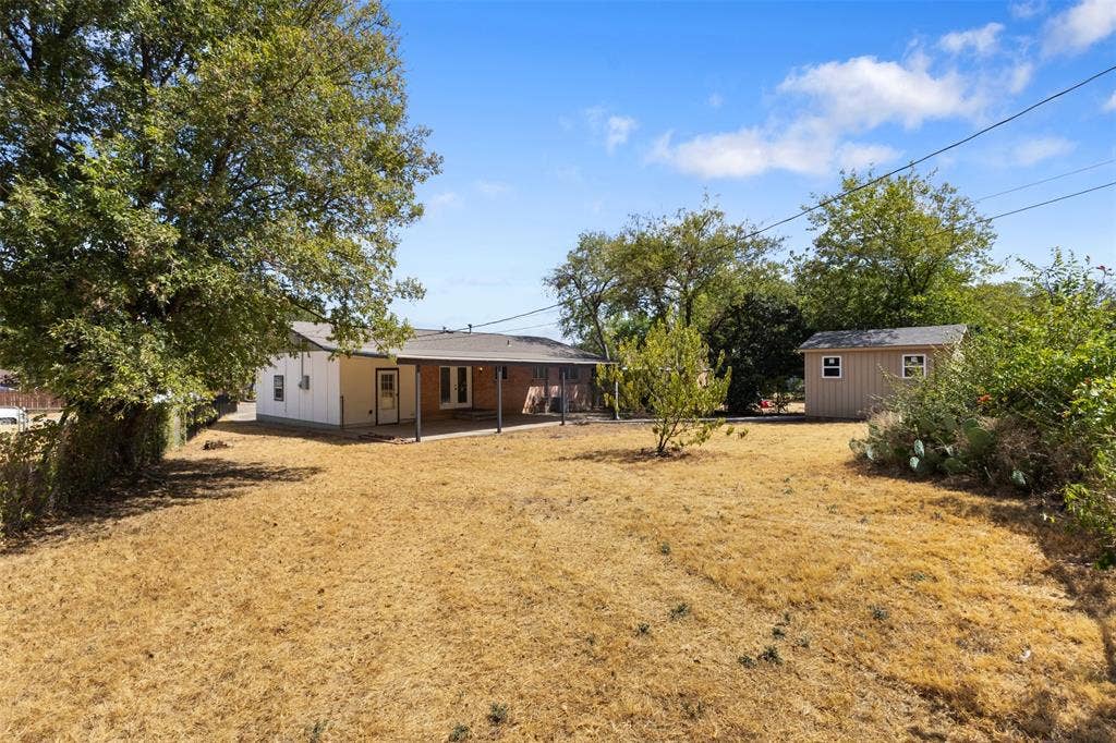 2563 Wood Valley Drive, Dallas, TX 75211 Expansive backyard featuring a covered patio, a detached storage shed with windows, and mature trees