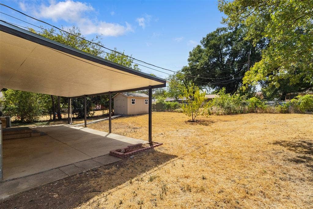 2563 Wood Valley Drive, Dallas, TX 75211 Covered concrete patio with metal support posts, complemented by a detached storage shed
