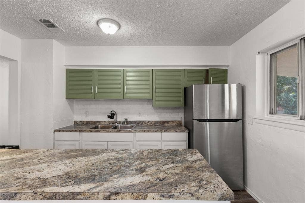2563 Wood Valley Drive, Dallas, TX 75211 Kitchen featuring stone countertops, a double basin sink, green louvered upper cabinetry, white lower cabinetry, and a stainless steel refrigerator