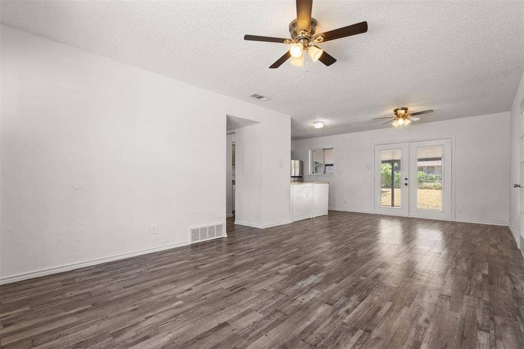 2563 Wood Valley Drive, Dallas, TX 75211 Spacious living area featuring wood-finish flooring, two ceiling fans, and double French doors providing access to the exterior