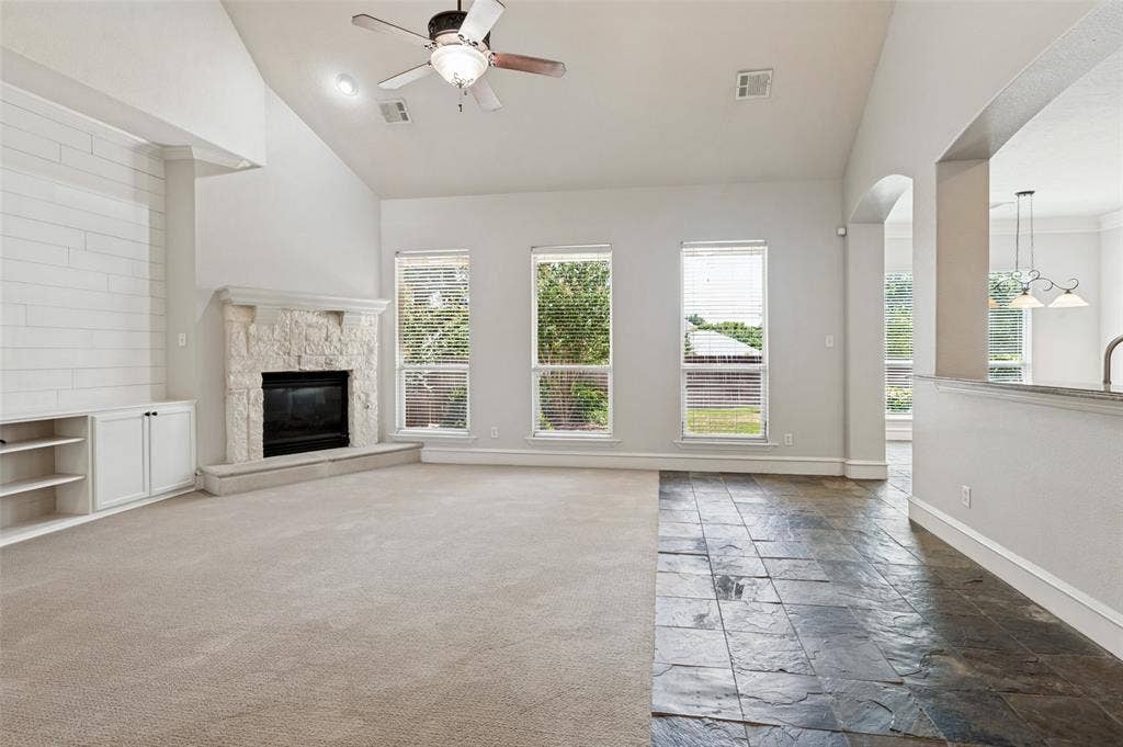 806 Cobblestone Court, Cedar Hill, TX 75104 Vaulted ceiling with a ceiling fan, stone-clad fireplace, built-in cabinetry, large windows, and a mix of carpet and stone tile flooring