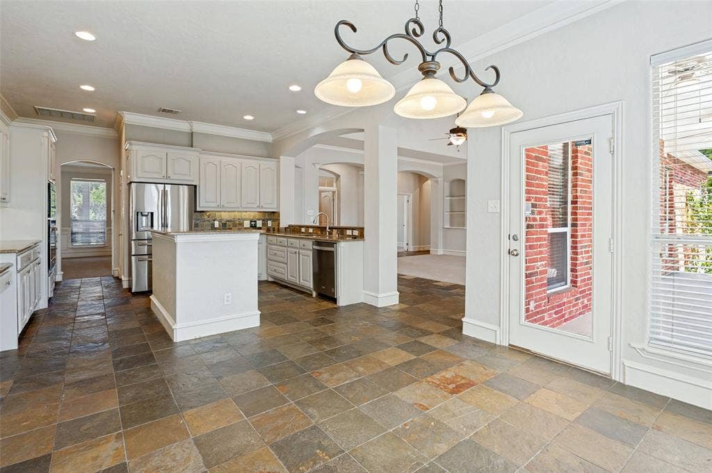 806 Cobblestone Court, Cedar Hill, TX 75104 Spacious kitchen featuring stone flooring, white cabinetry, a kitchen island, stainless steel appliances, and a glass-paneled exterior door