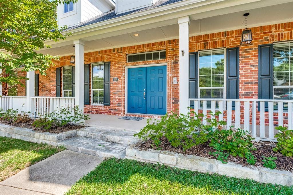 806 Cobblestone Court, Cedar Hill, TX 75104 Brick exterior with a covered porch, white railing, and a vibrant blue double entry door