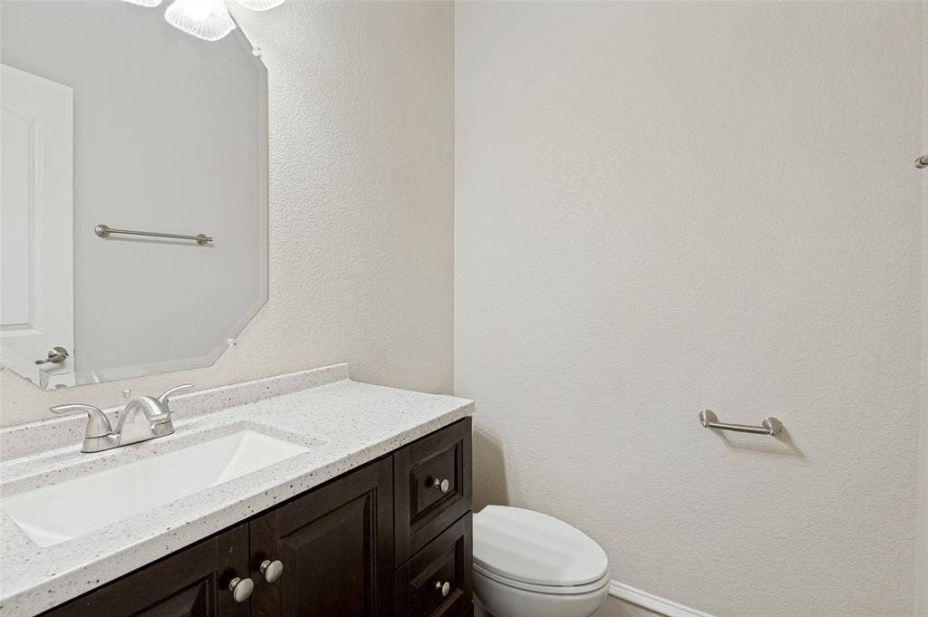 806 Cobblestone Court, Cedar Hill, TX 75104 Dark wood-finish vanity with an integrated sink, light-toned countertop, brushed nickel faucet, and an octagonal mirror