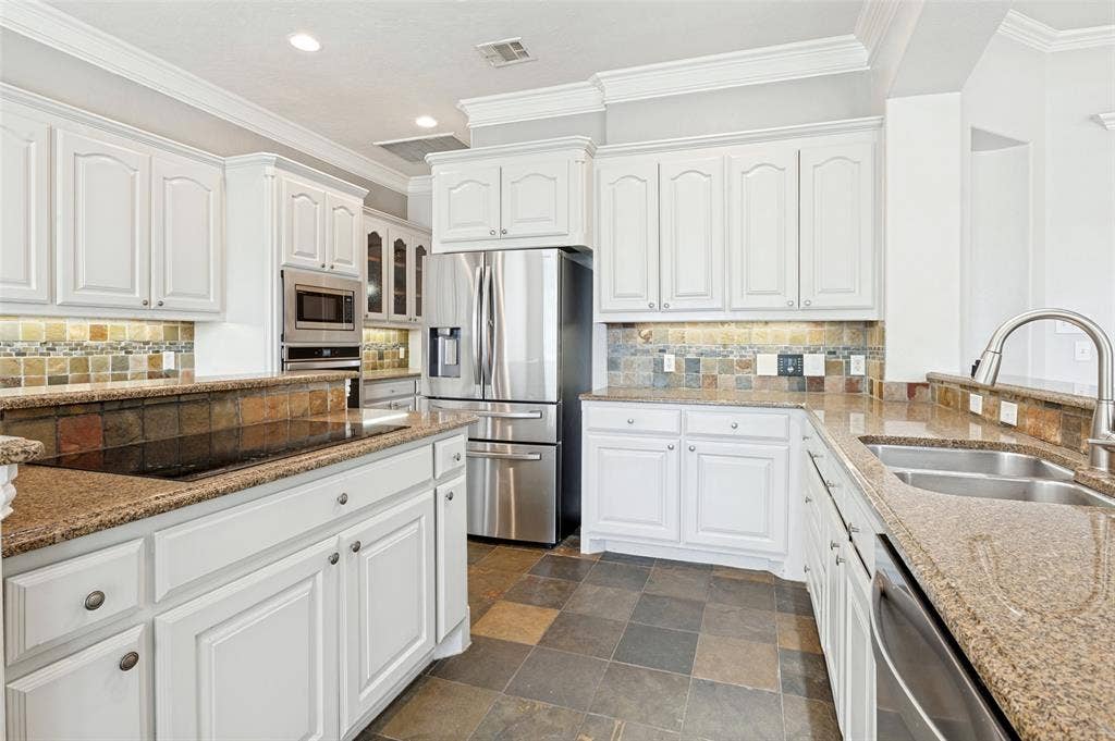 806 Cobblestone Court, Cedar Hill, TX 75104 White cabinetry, stainless steel appliances, stone tile flooring, granite countertops, and a decorative tile backsplash