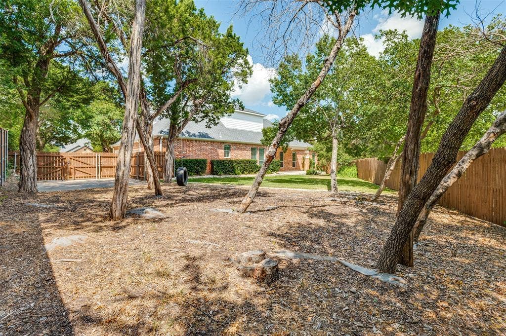 806 Cobblestone Court, Cedar Hill, TX 75104 Expansive backyard with multiple mature trees, a wood privacy fence, and a brick exterior dwelling visible in the background