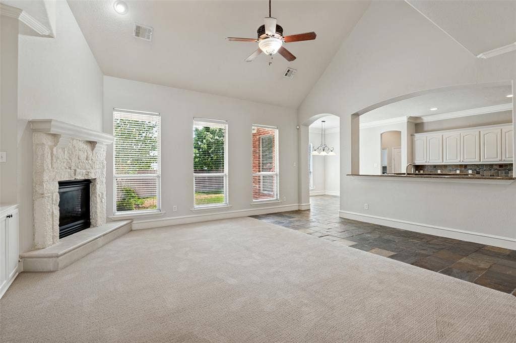 806 Cobblestone Court, Cedar Hill, TX 75104 Vaulted ceilings, a stone-clad fireplace, and a ceiling fan enhance the living area, while a breakfast bar with white cabinetry and a tile backsplash separates the kitchen space