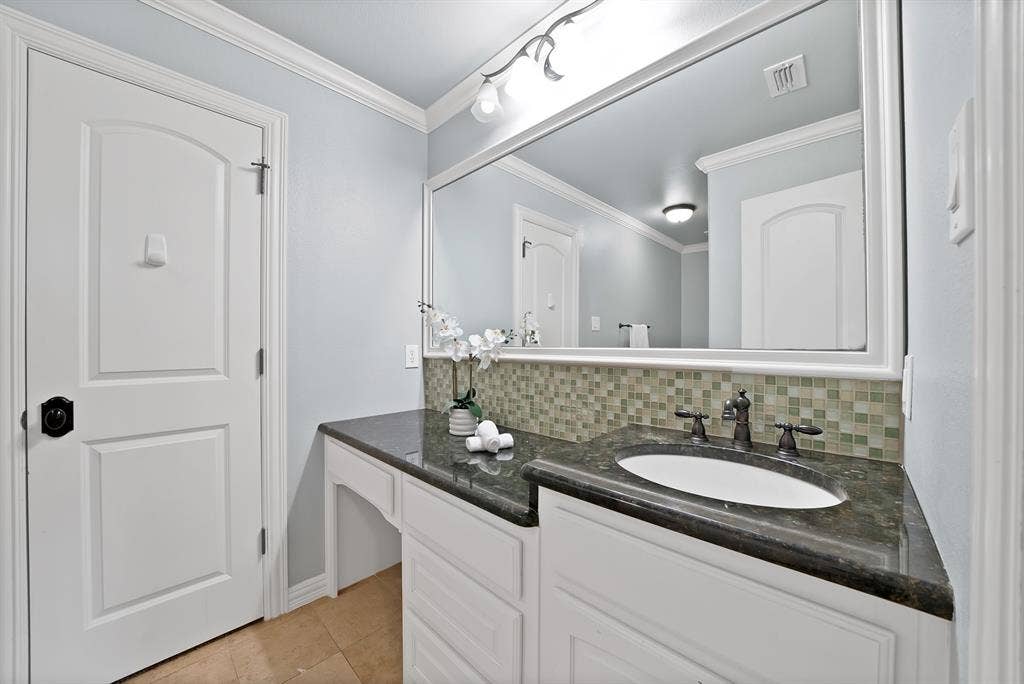 Spacious vanity with an integrated sink, dark countertop, and mosaic tile backsplash