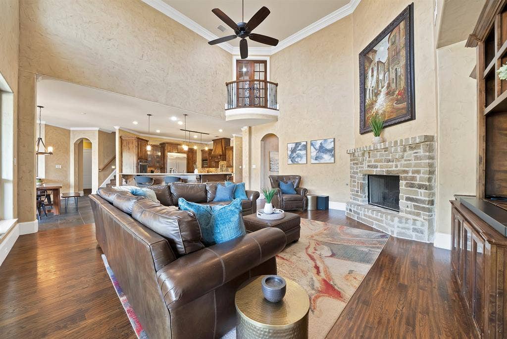Expansive living area with high ceilings, a balcony overlook, a stone fireplace, hand scraped hardwood floors, and a ceiling fan