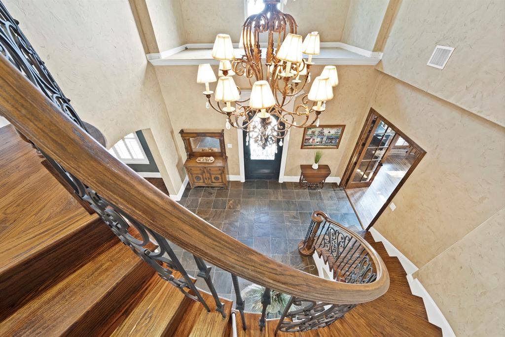 High ceilings with a decorative chandelier, tile flooring, hand scraped hardwood staircase with wrought iron balusters, and an arched entryway