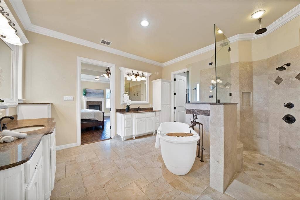 Dual vanity with integrated sinks, freestanding soaking tub, and a glass-enclosed walk-in shower with multiple shower heads