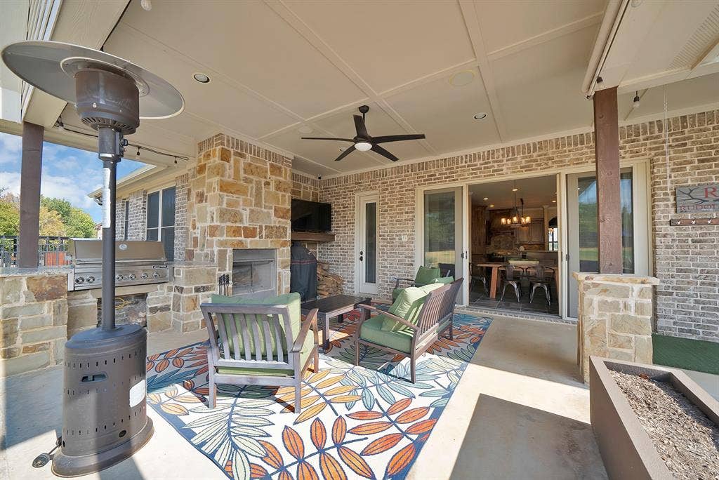 Covered patio featuring a stone fireplace, built-in outdoor grill, ceiling fan, and sliding glass doors