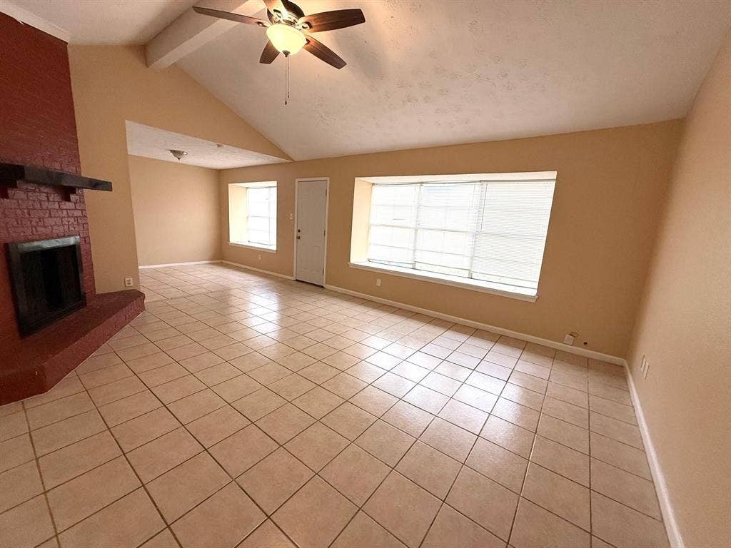 2705 Tanglewood Drive, Lancaster, TX 75134 Vaulted ceilings with exposed beam, ceramic tile flooring, brick fireplace with wood mantel, ceiling fan with light fixture, and window with blinds