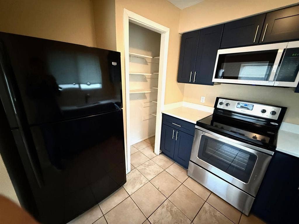 2705 Tanglewood Drive, Lancaster, TX 75134 Kitchen featuring stainless steel range, built-in microwave, dark blue cabinetry, light countertops, and tile flooring