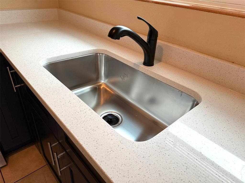 2705 Tanglewood Drive, Lancaster, TX 75134 Undermount stainless steel sink with a matte black faucet, set within a light-toned countertop with integrated backsplash
